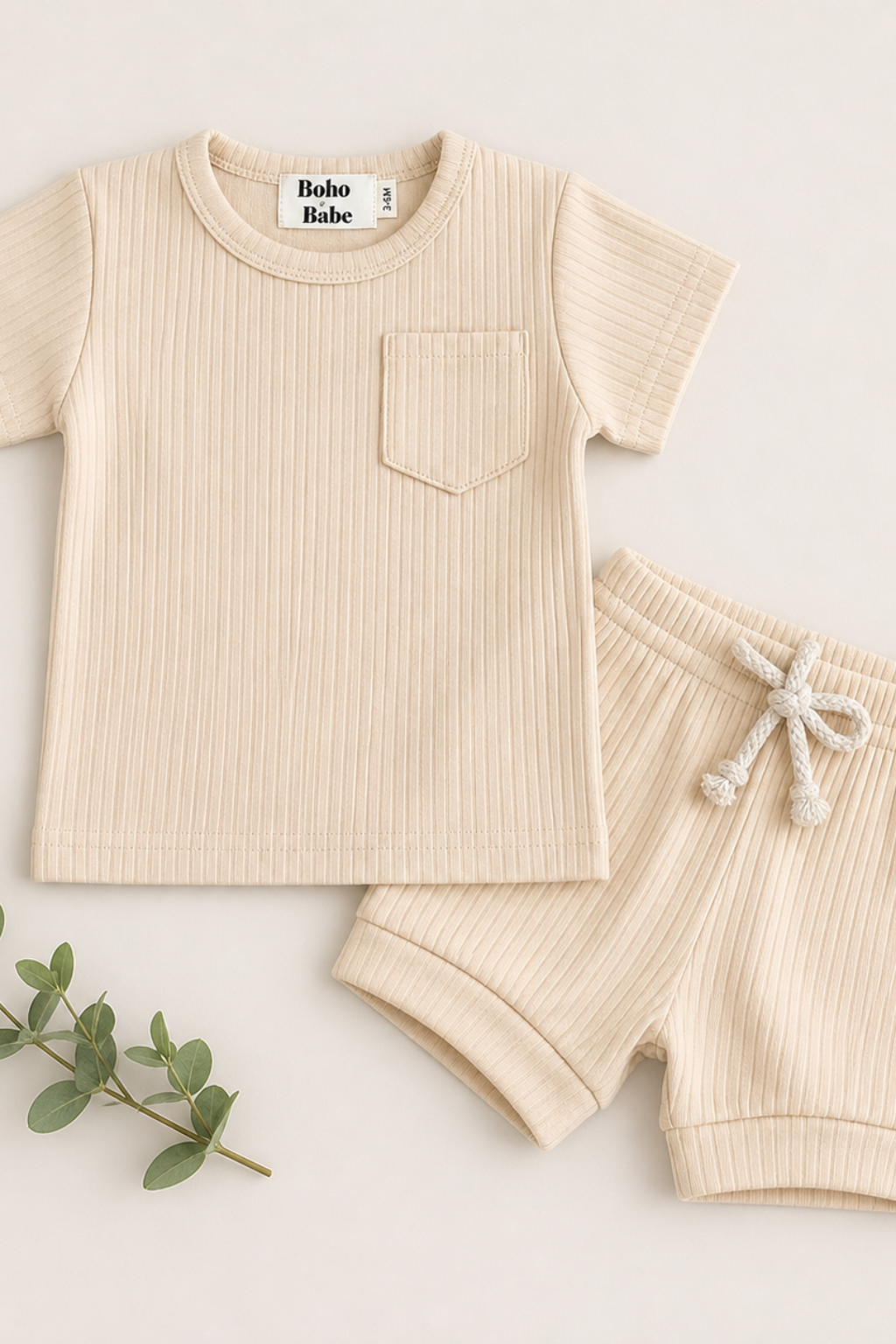 A baby two-piece outfit set featuring a short-sleeve ribbed knit top with a chest pocket and matching ribbed knit shorts with a drawstring, in a light cream color. The brand label 'Boho Babe' is visible inside the collar.